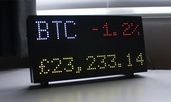LED Crypto Ticker Display auf einem Schreibtisch mit Münzen
